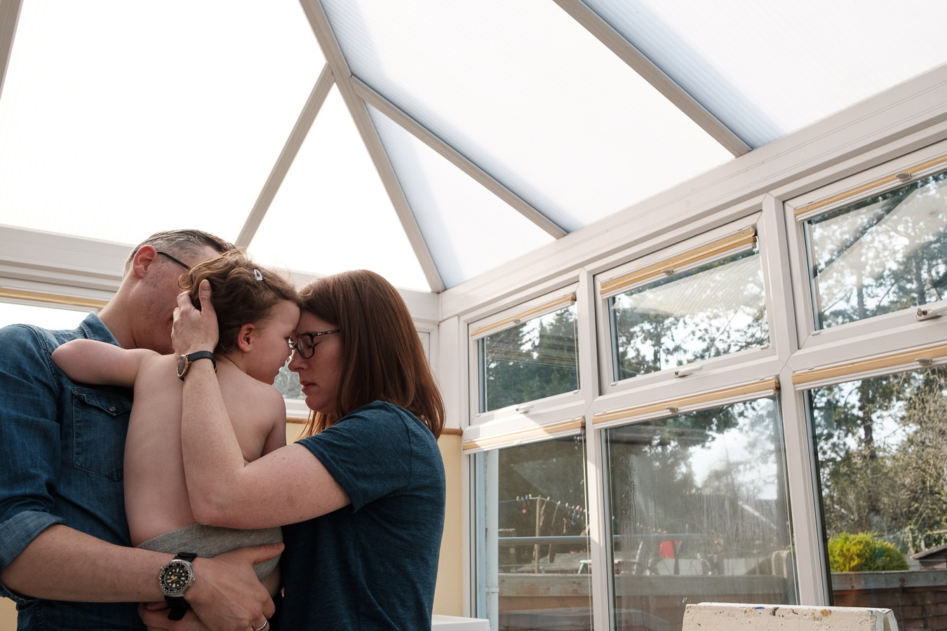 Family of parents and daughter embracing in conservatory.