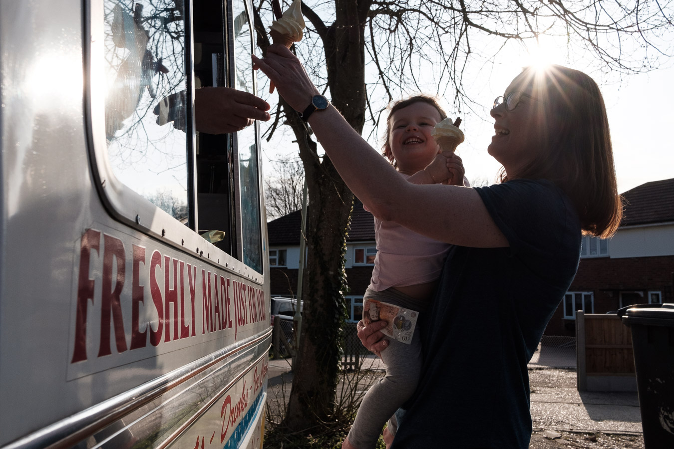 mum and daughter buy an ice cream from a van parked by their house.