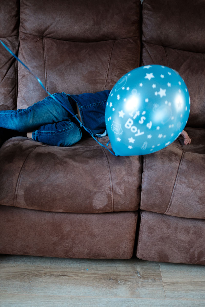 Boy hiding behind ballon on sofa