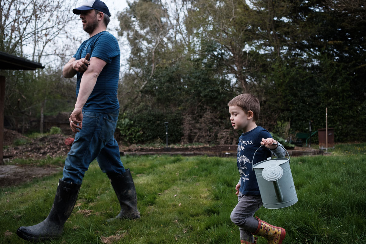son and father walking together with watering can in garden.