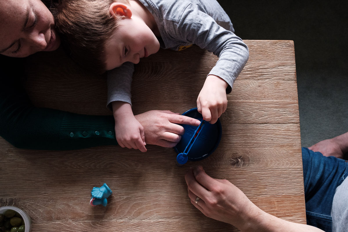 Child playing board game with parents hands showing.