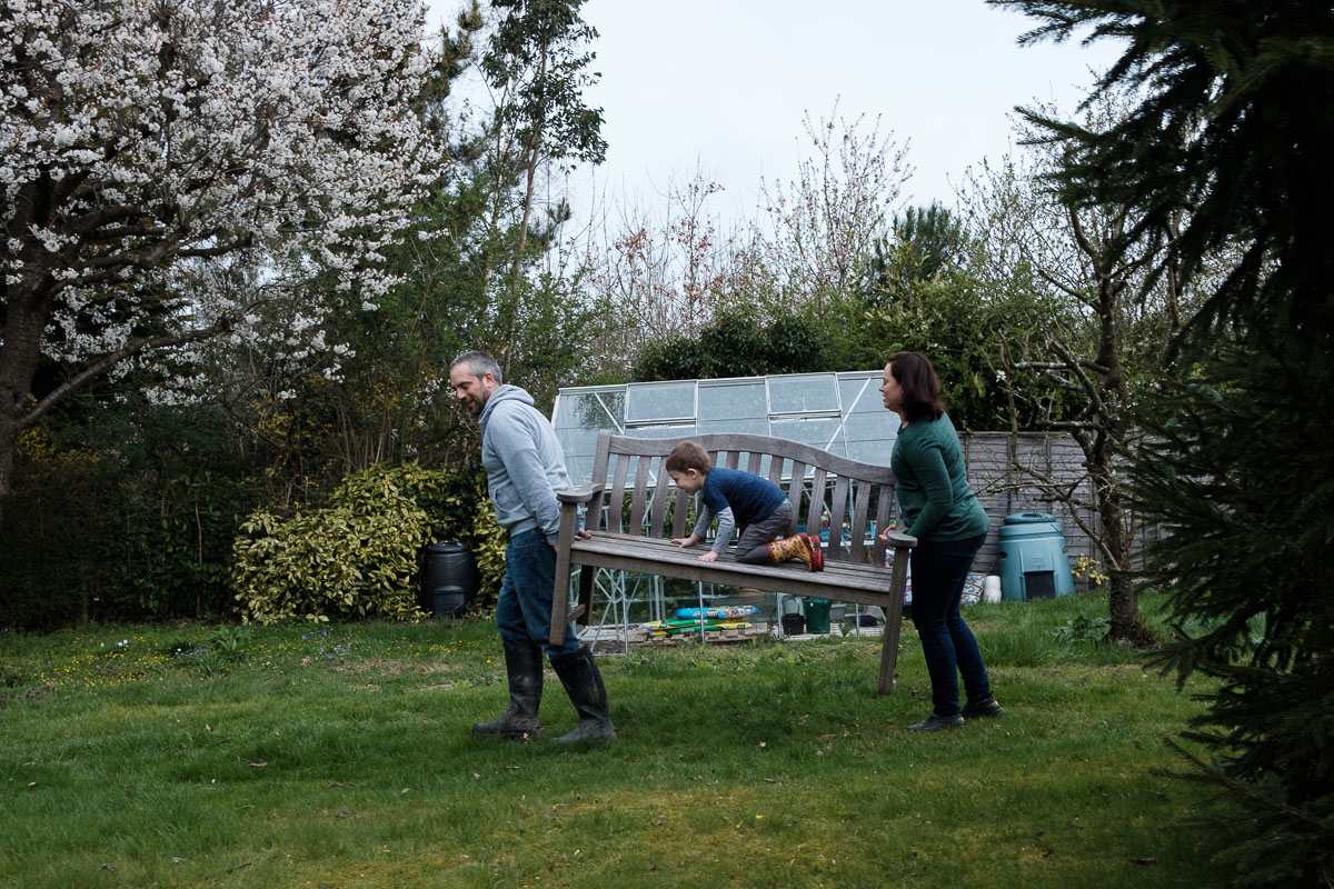Couple carrying bench in garden.