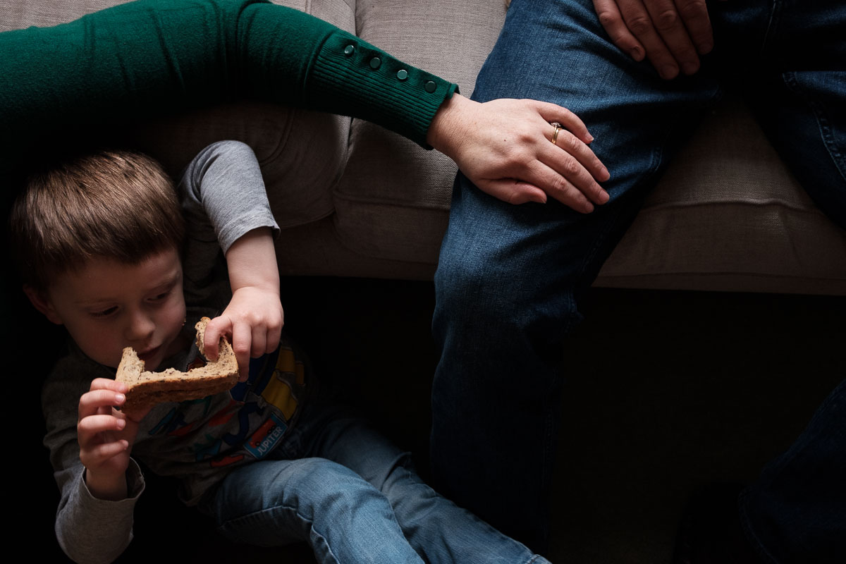 boy eats a sandwich with his mum and dad in living room.