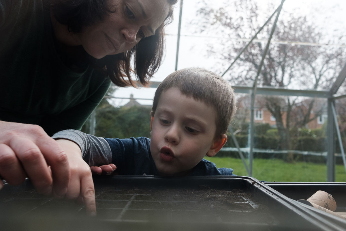 Mother and son plant seeds in their greenhouse.
