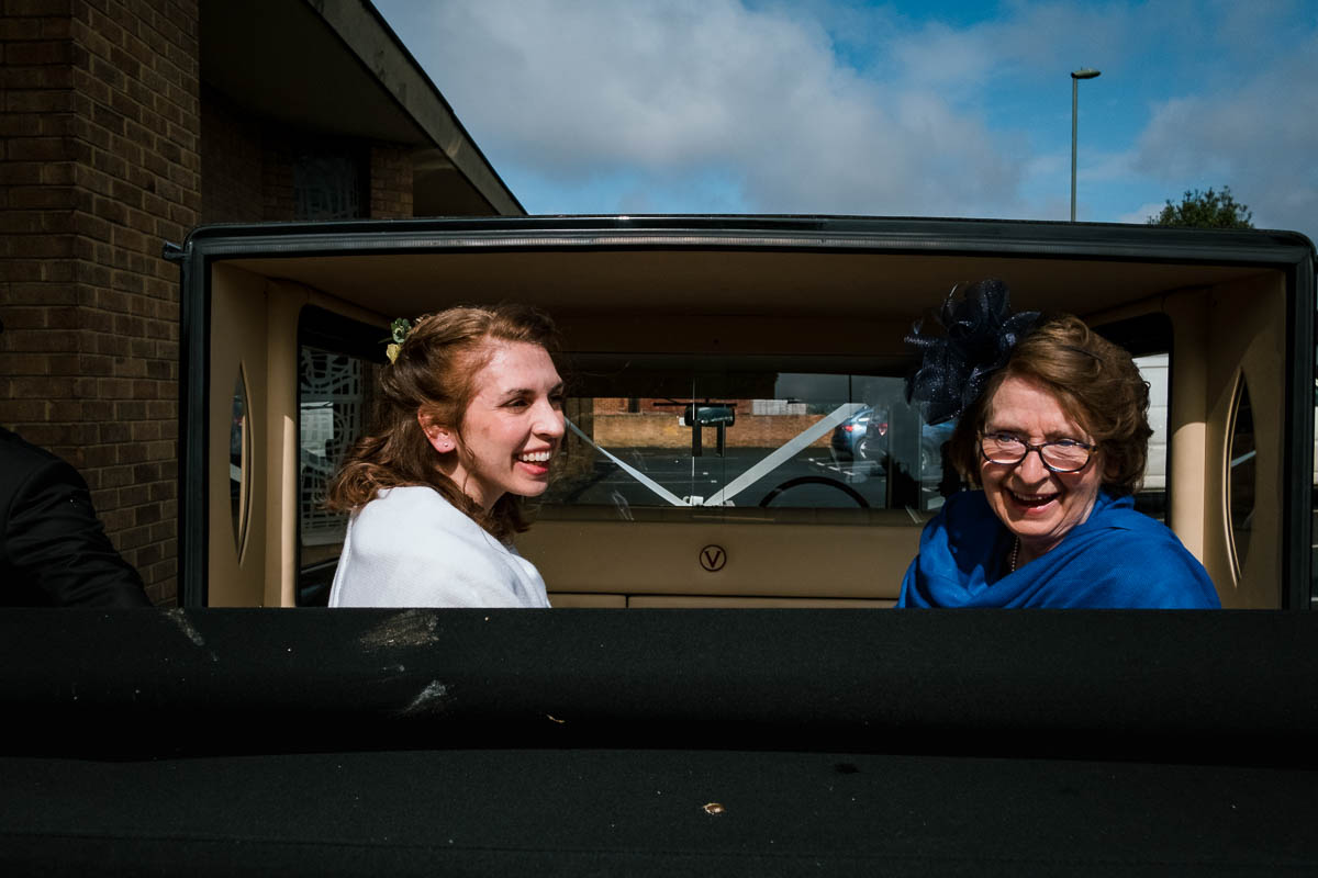 Bride and mother smiling inside car by church